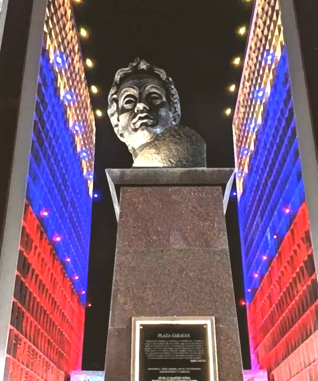 Plaza Caracas de noche: un busto de bronce sobre su pedestal de granito, entre las dos torres iluminadas del Centro Simón Bolívar